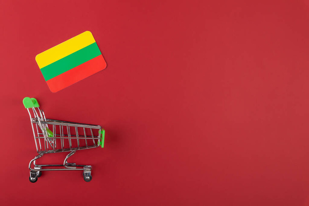 Mini empty supermarket shopping grocery cart, Lithuania, Bolivia flag on red background - Foto, Imagem