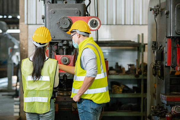 Azjatycki mężczyzna i kobieta inżynieria nosić ochrona twarz maska i kask bezpieczeństwa pracy przodu maszyny w fabryce Przemysłowe. nowa normalna praca podczas epidemii covid-19. - Zdjęcie, obraz