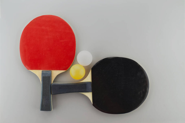 Two table tennis racks with a white and yellow ping pong ball on grey background - Φωτογραφία, εικόνα
