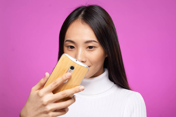 aranyos ázsiai megjelenés telefon a kézben internet kommunikációs technológia rózsaszín háttér - Fotó, kép