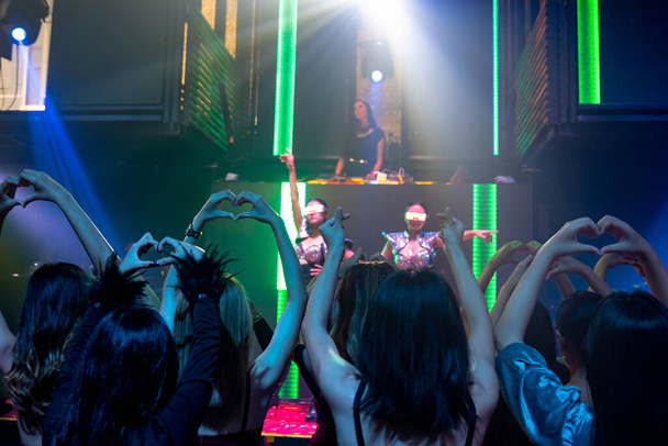 Группа людей танцует в дискотечном ночном клубе под ритм музыки от DJ на сцене - Фото, изображение