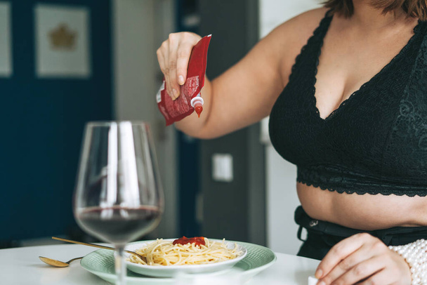 Mujer joven más cuerpo de tamaño positivo con plato de pasta y ketchup almorzando en la casa - Foto, Imagen