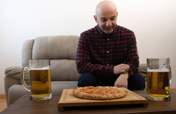 Junger Mann mit Bier und Pizza im Zimmer  - Foto, Bild
