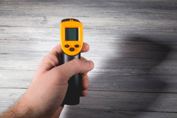 Um homem tem um pirômetro amarelo-preto sobre um fundo de madeira. Um dispositivo para medição de temperatura sem contacto. Estúdio foto. - Foto, Imagem