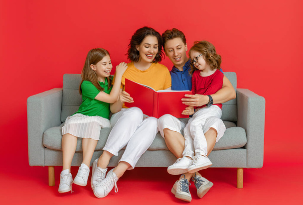 Happy loving family. Mother, father and children daughters reading a book on red background.  - Fotografie, Obrázek