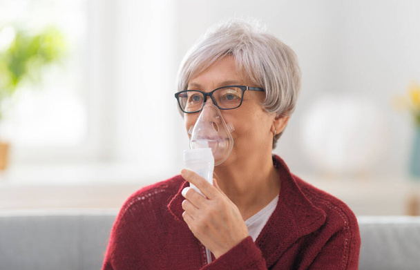 Elderly woman using inhaler for asthma and respiratory diseases at home. - Foto, imagen