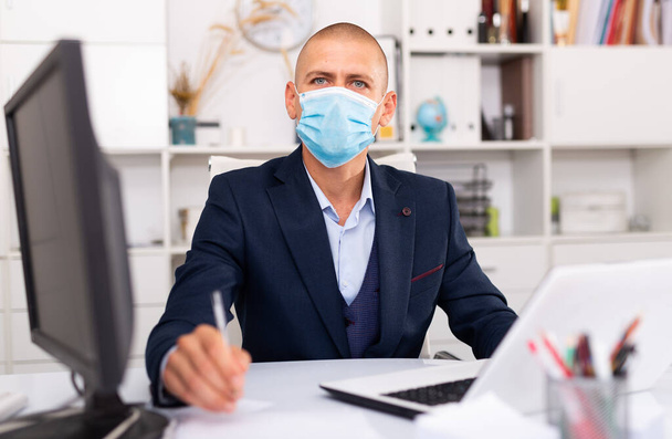 Professional business man in protective medical mask using laptop at workplace - Photo, Image