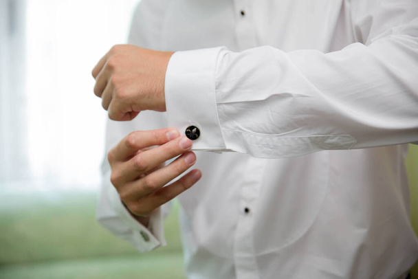 közelkép egy férfi kezéről, amint egy mandzsettagombot rögzít a fehér ingére. - Fotó, kép