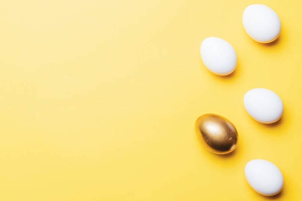 イースターパターン。ハッピーイースターの装飾でパステルイエローの背景に黄金、白い色の卵。春休み｜Top view Concept - 写真・画像