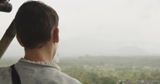 Close up tiro de um homem observando o vale abaixo de uma cabana de observação e bagunçando seu cabelo castanho com a mão - Filmagem, Vídeo