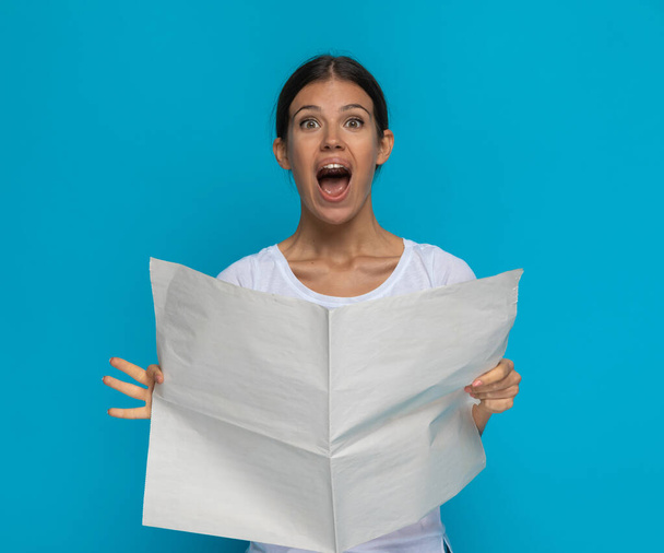 beautiful casual woman feeling excited after reading the newspaper against blue background - Photo, image