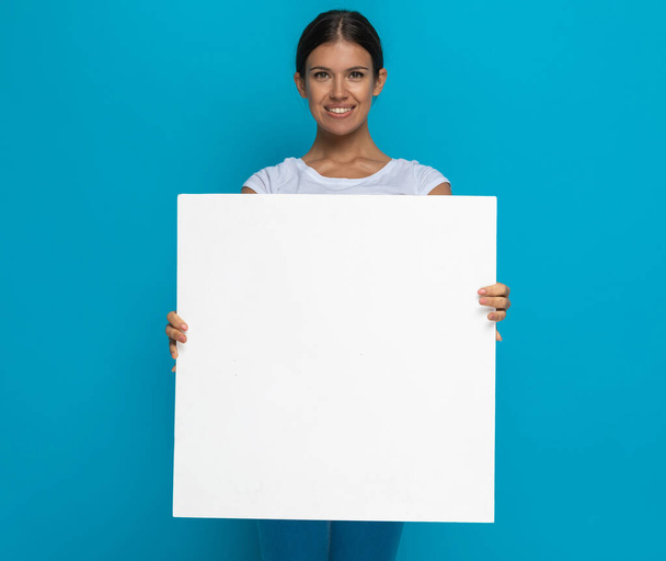 happy casual woman presenting her billboard at the camera against blue background - Photo, Image