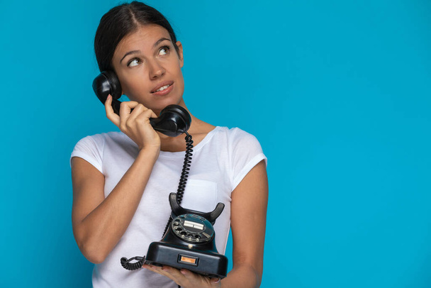 szexi alkalmi nő beszél a telefonon, és gondolkodás valami ellen kék háttér - Fotó, kép