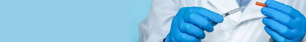 Lékařská ruka v ochranných lékařských rukavicích drží inzulínovou stříkačku na modrém pozadí. Příprava inzulínu, koronavirová vakcína, vakcína proti chřipce, subkutánní injekce, prevence imunizace - Fotografie, Obrázek