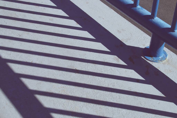 Тень решетки перила на улице в Мадриде, Испания. Серый пол с тенью металлических прутьев в перспективе. - Фото, изображение