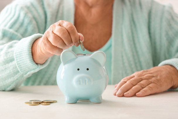 Senior woman putting coin into piggy bank at table. Concept of pension - Photo, Image
