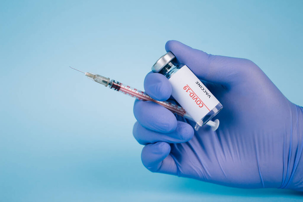 Doctor or scientist holding vial dose of COVID-19 vaccine with syringe against blue background with copy space for text - prevention coronavirus, global vaccination concept. Selective focus - Photo, Image
