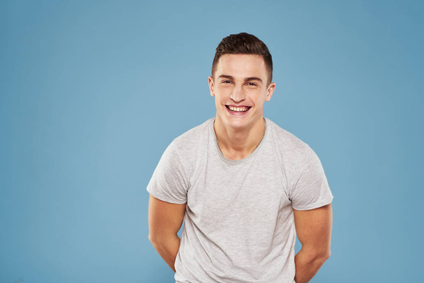 cheerful man in a white t-shirt gesturing with his hands emotions blue background - Foto, Bild