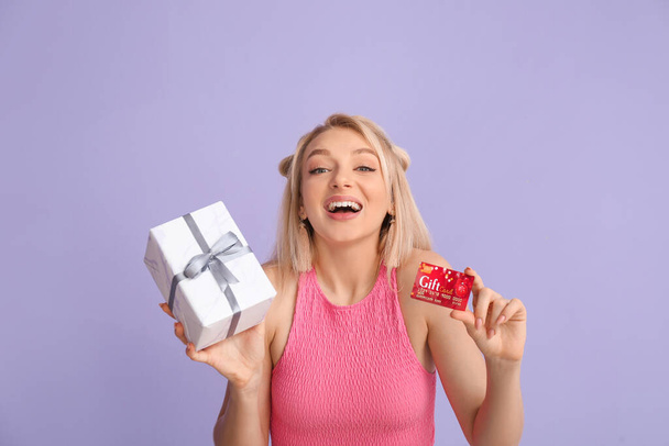 Красива молода жінка з подарунковою карткою і подарунком на кольоровому фоні
 - Фото, зображення