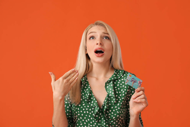 Aggódó fiatal nő ajándékkártyával színes háttér - Fotó, kép