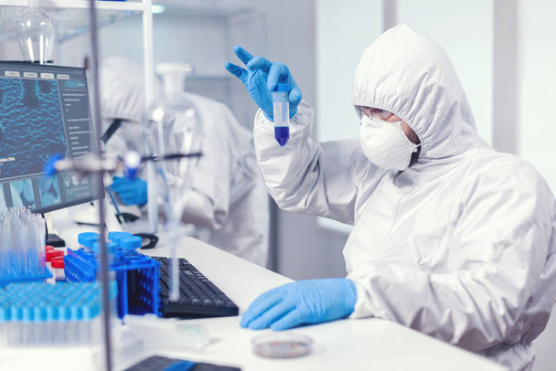 Naukowiec w pokrywach laboratoryjnych przyglądający się dokładnie próbce w probówce - Zdjęcie, obraz