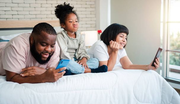 Les filles afro-américaines ne sont pas satisfaites et tristes, assis au milieu entre le père et la mère. Les parents utilisent le smartphone et les enfants abandonnés. Les enfants ont besoin de l'attention des parents. - Photo, image
