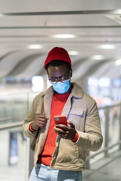 Homem preto usando telefone inteligente no terminal do aeroporto, usar máscara médica rosto, usando celular. Covid-19. - Foto, Imagem