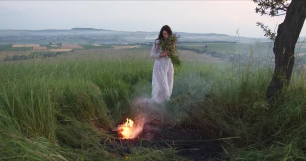 mooi meisje gooit een boeket van wilde bloemen in het vuur - Video