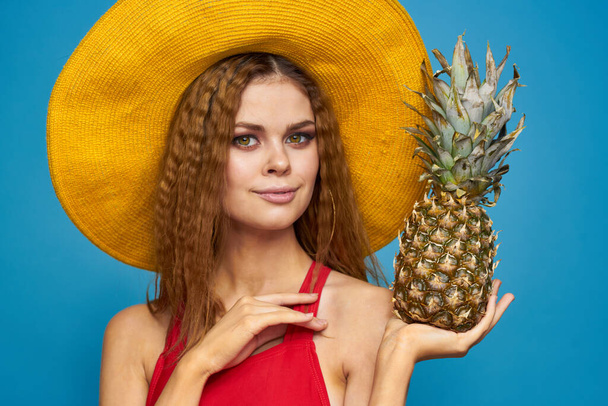 Mujer en sombrero amarillo con piña en las manos emociones estilo de vida divertido fruta de verano fondo azul - Foto, Imagen