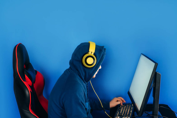 O jogador senta-se em uma cadeira de jogo e joga jogos de computador. O jogador tem fones de ouvido amarelos na cabeça. - Foto, Imagem
