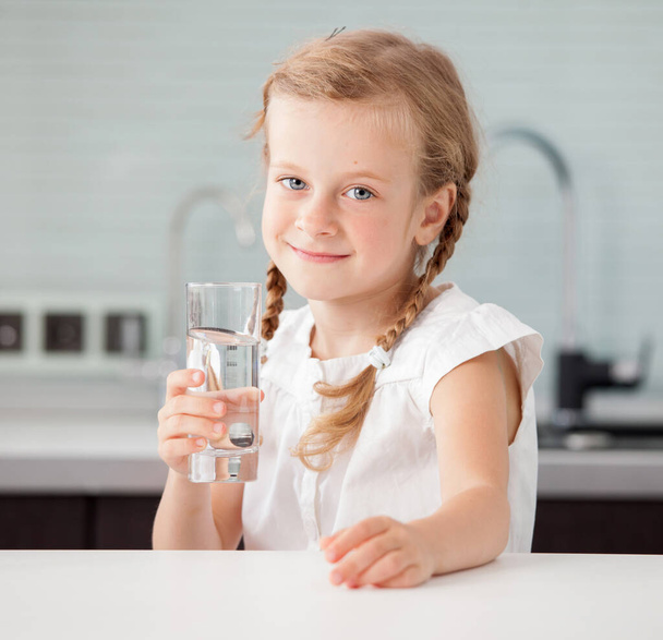 Child drinking water from glass. Happy little girl at home in kitchen - Foto, imagen