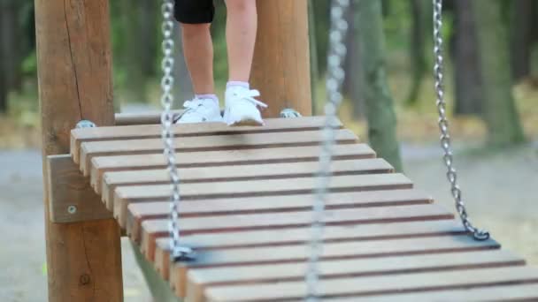 公園の遊び場で揺れる木製の橋の上の子供たちの足のクローズアップ。子供たちは子供の遊び場で遊ぶ。集中力を失い - 映像、動画