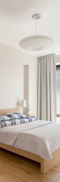 Panorama vertical de dormitorio cómodo y luminoso con cama grande y lámpara de techo con estilo - Foto, imagen