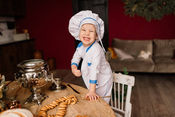 Petite cuisinière mignonne avec couverts assise sur la cuisine, frères jumeaux, mandarine, bagels - Photo, image
