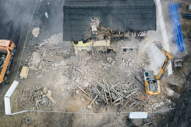 黄色の掘削機は建物を破壊する。ヘビーデューティ機器はレンガ造りの建物を破壊しています。建物の取り壊しだ。解体工事空中ドローンフォトビュー - 写真・画像