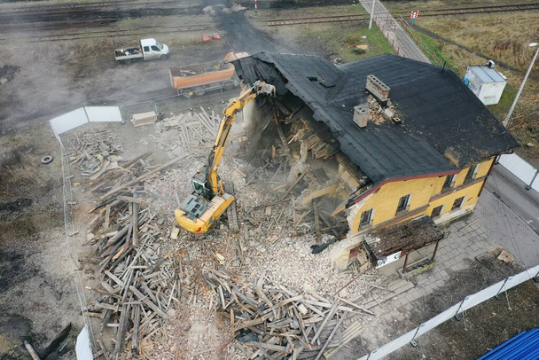 黄色の掘削機は建物を破壊する。ヘビーデューティ機器はレンガ造りの建物を破壊しています。建物の取り壊しだ。解体工事空中ドローンフォトビュー - 写真・画像