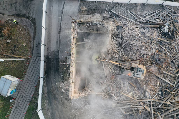 Scavatore giallo distrugge edificio. La macchina pesante sta demolendo un edificio in mattoni. Demolizione dell'edificio. Demolizione lavori di costruzione aereo drone foto vista - Foto, immagini