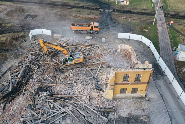 Żółty koparka niszczy budynek. Ciężka maszyna burzy budynek z cegły. Rozbiórka budynku. Budowa prac rozbiórkowych dron powietrzny widok zdjęcia - Zdjęcie, obraz