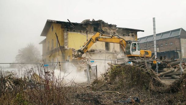 A sárga kotrógép lerombolja az épületet. A nagy teherbírású gép lerombol egy téglaépületet. Az épület lerombolása. Robbantási munkálatok légi drónkép megtekintése - Fotó, kép