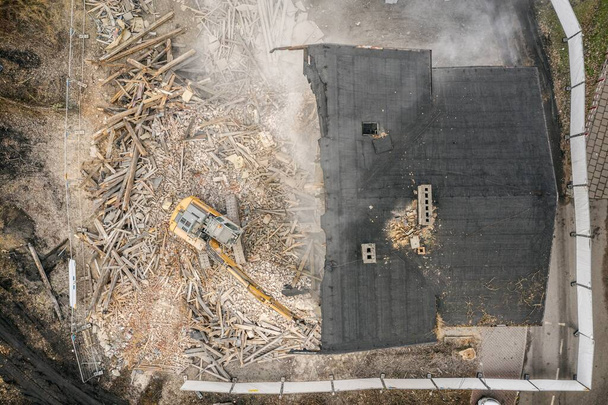 A sárga kotrógép lerombolja az épületet. A nagy teherbírású gép lerombol egy téglaépületet. Az épület lerombolása. Robbantási munkálatok légi drónkép megtekintése - Fotó, kép