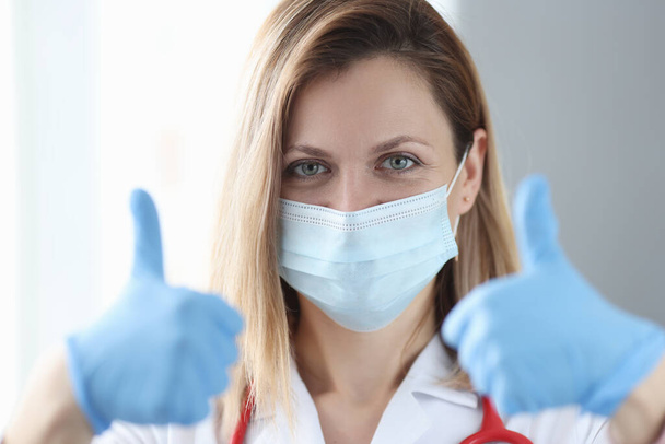 Жінка-лікар в захисній медичній масці показує великий палець вгору
 - Фото, зображення