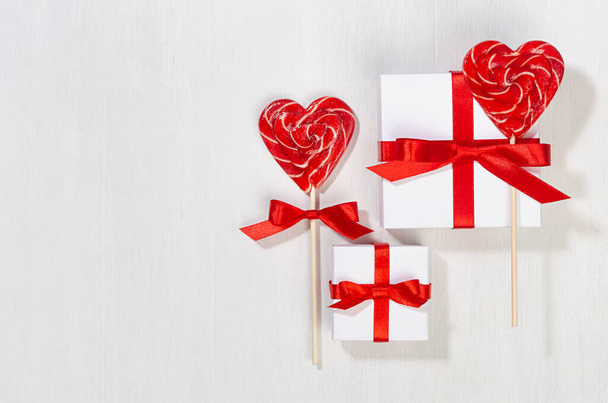 Fun valentines day background - white gift boxes with red silk bow, sweet lollipops hearts on white wood board, copy space. - Φωτογραφία, εικόνα