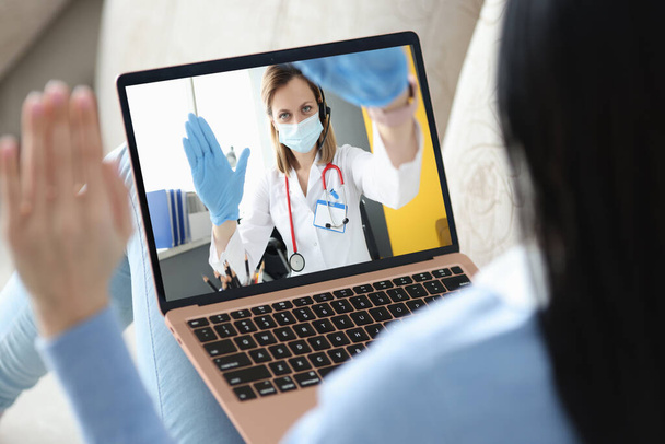 Doctor wearing mask and gloves communicating with patient via laptop - Foto, Bild