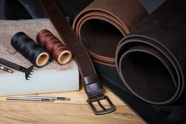 Herramientas de fabricación de cuero con cinturón hecho a mano en una tabla de troquelado usada. Conjunto de herramientas artesanales de cuero (herramientas de bricolaje) sobre un fondo oscuro - Foto, Imagen