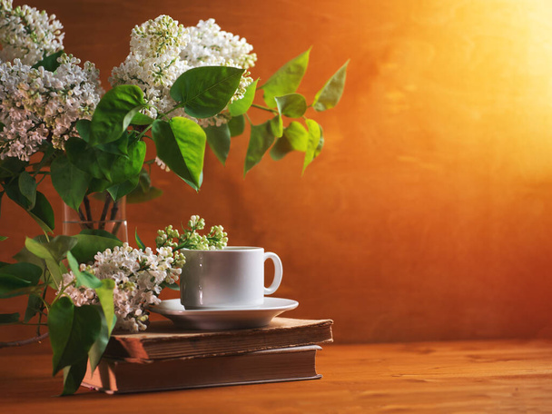 Egy csésze illatos tea vagy kávé, egy virágzó fehér csokor orral és régi könyvekkel. - Fotó, kép