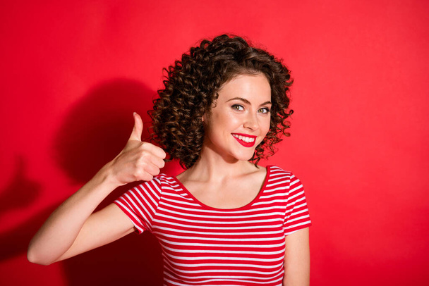 Photo of stunning pretty curly young lady wear casual striped outfit showing thumb up isolated red color background - Foto, afbeelding