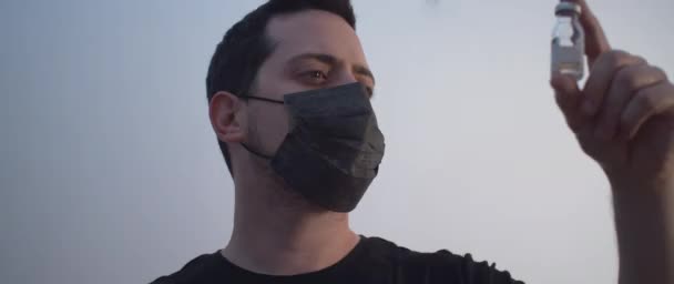 A man wearing a black mask holding a bottle of Vaccine - Footage, Video