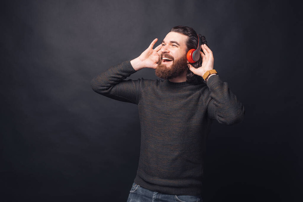 Fénykép boldog jóképű férfi hallgat zenét fejhallgató felett fekete háttér - Fotó, kép