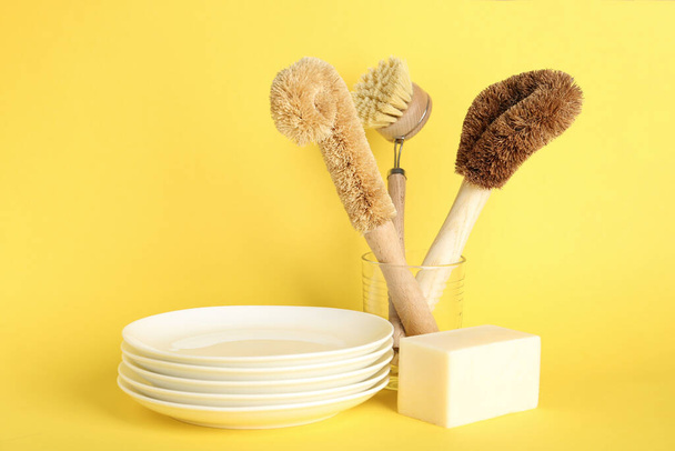 Cleaning supplies for dish washing and plates on yellow background - Fotografie, Obrázek
