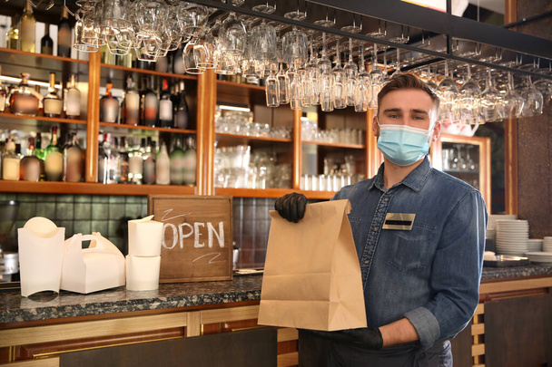 Waiter with packed takeout order in restaurant. Food service during coronavirus quarantine - Foto, imagen